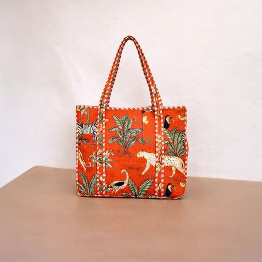 Orange tote bag with animal and plant pattern on a beige surface